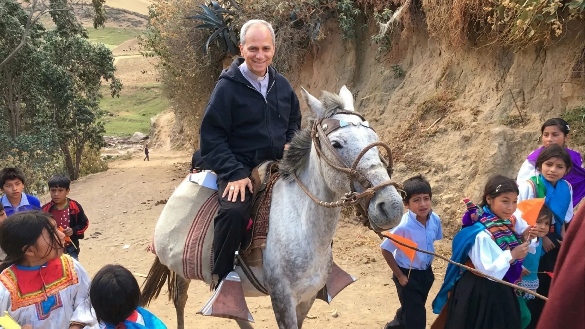 Robert Prevost a caballo por un camino de tierra, rodeado de niños con trajes típicos